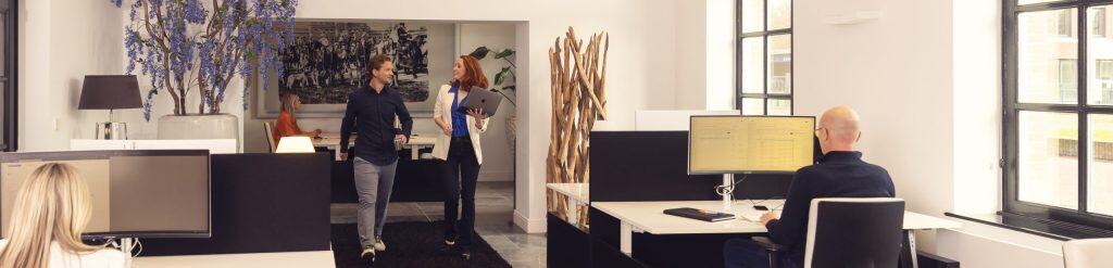 Moderne kantoorruimte met open werkplekken en collega’s in gesprek.